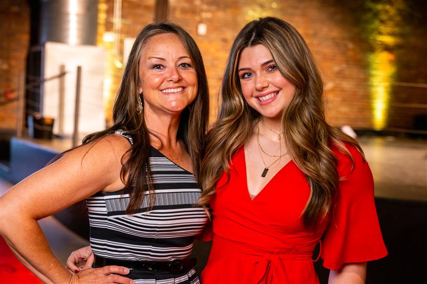 A woman wearing a black and white dress and a woman wearing a red dress smile
